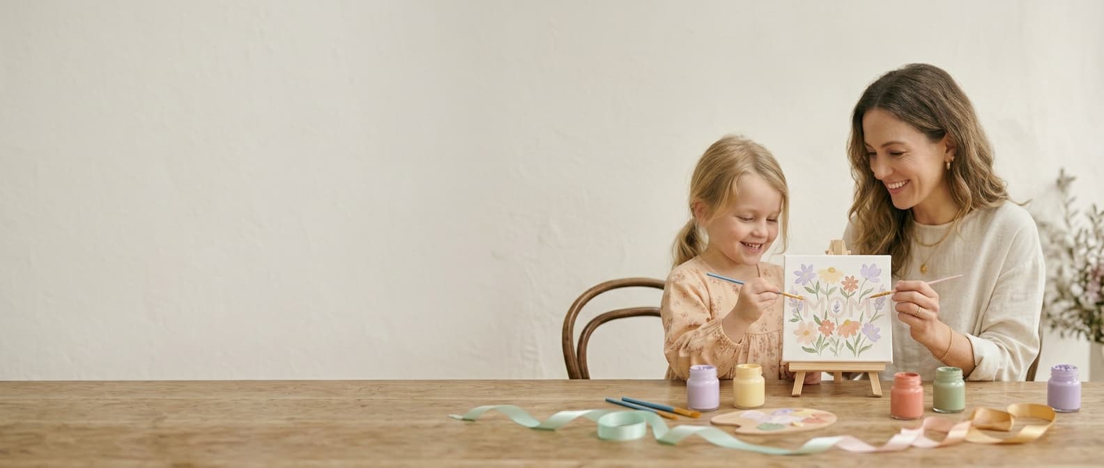 Mom and daughter wearing superhero capes, excitedly opening a Wonder Mom Box together
